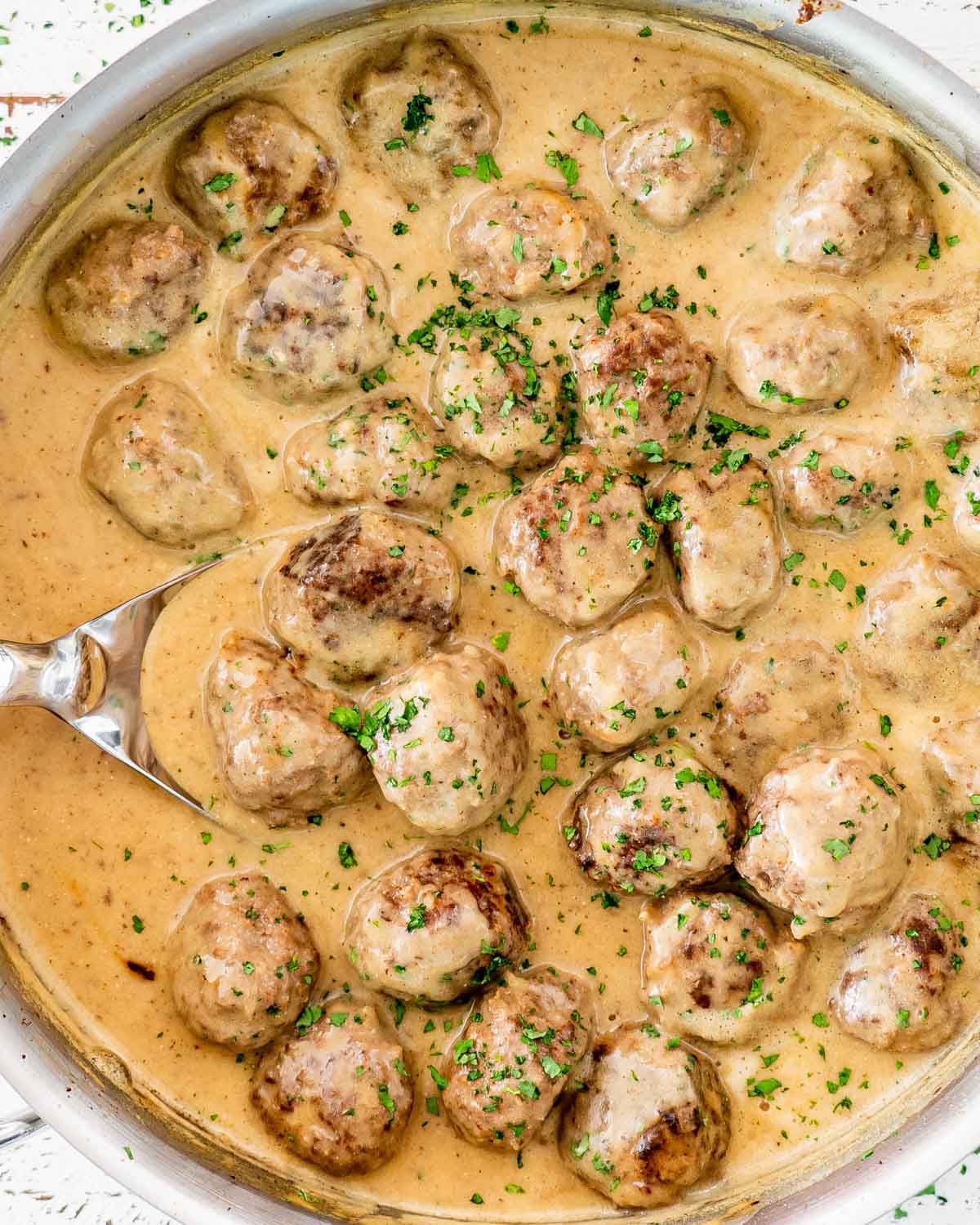 swedish meatballs with gravy in a skillet with a spoon in it.