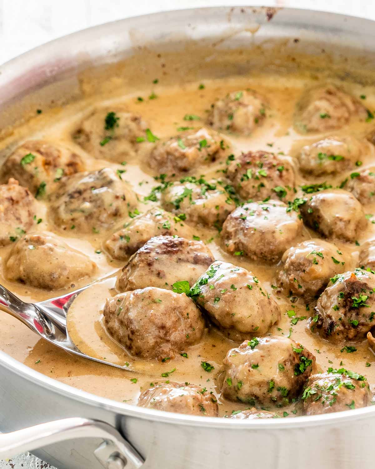 swedish meatballs with gravy in a skillet with a spoon in it.