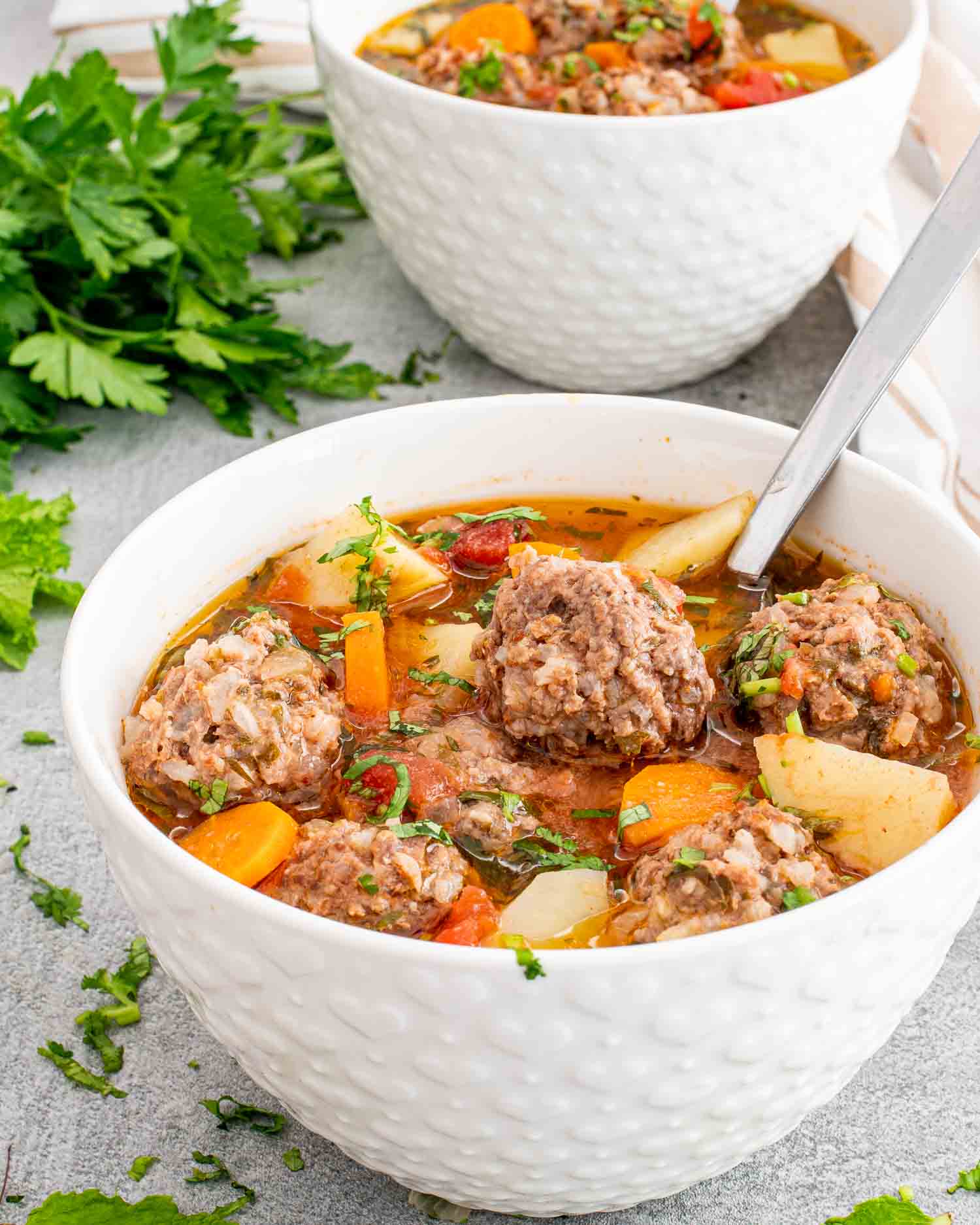 albondigas soup in a white bowl with a spoon inside.