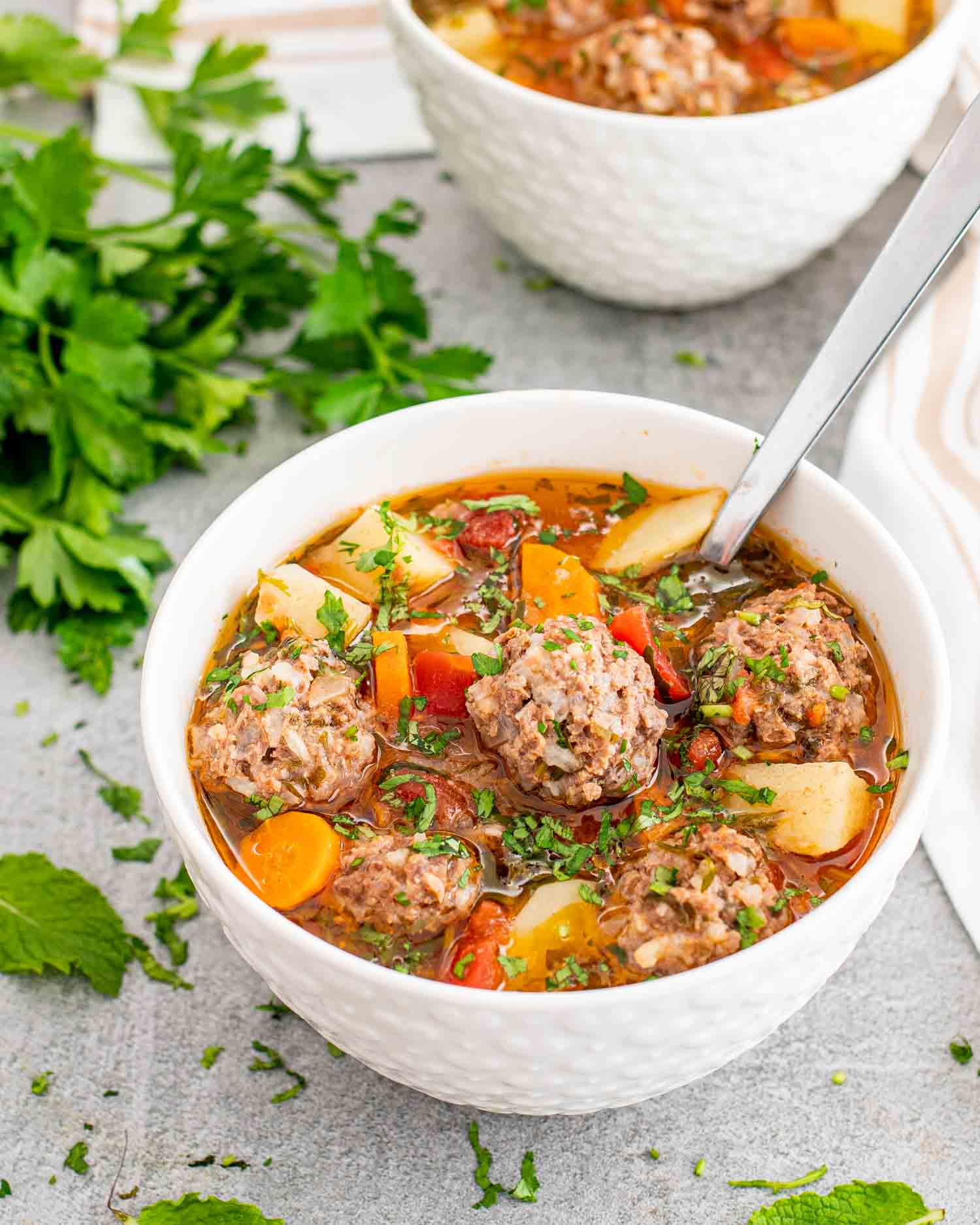 albondigas soup in a white bowl with a spoon inside.