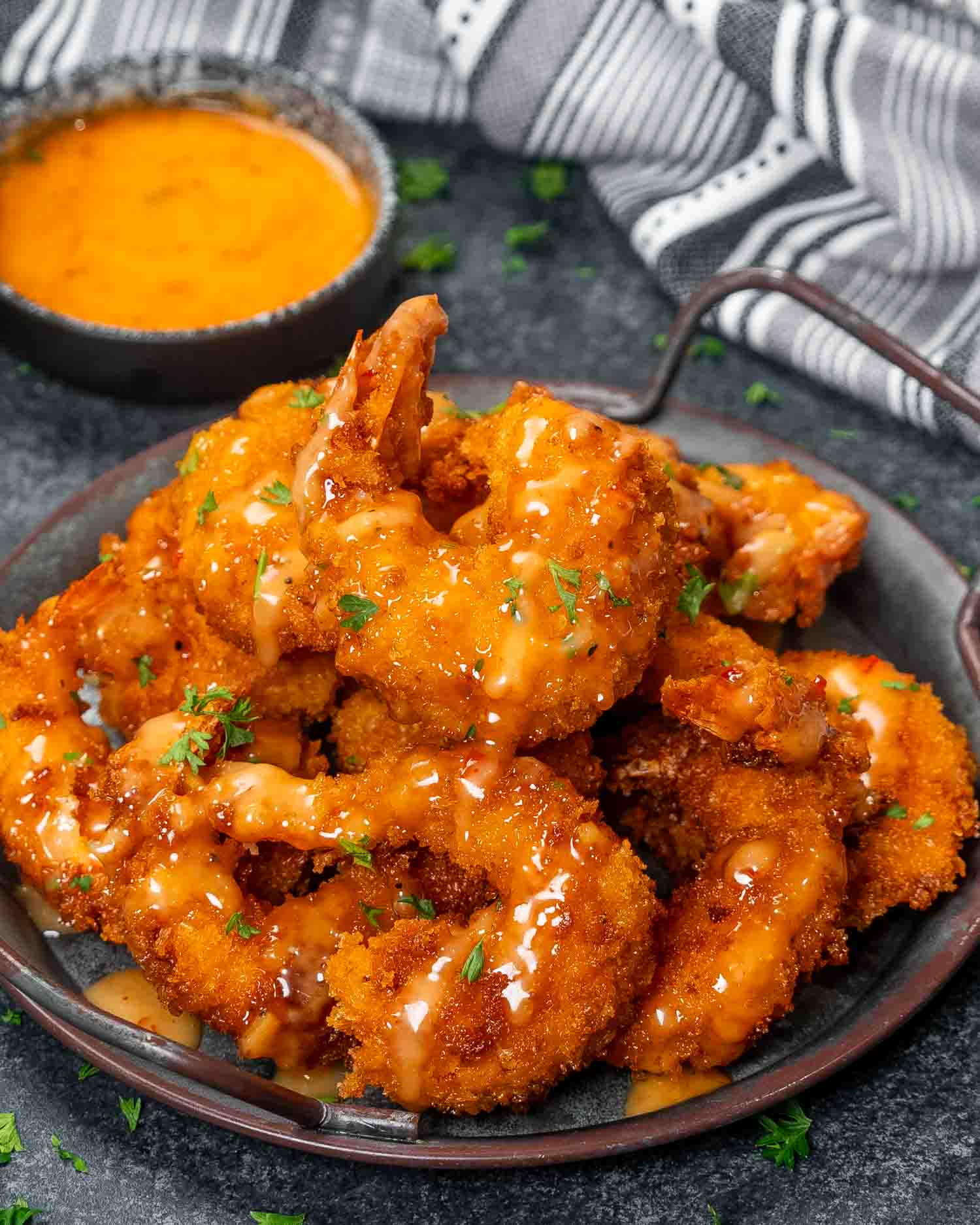 a metal plate filled with bang bang shrimp, crispy and fried and drizzled with a delicious bang bang sauce.