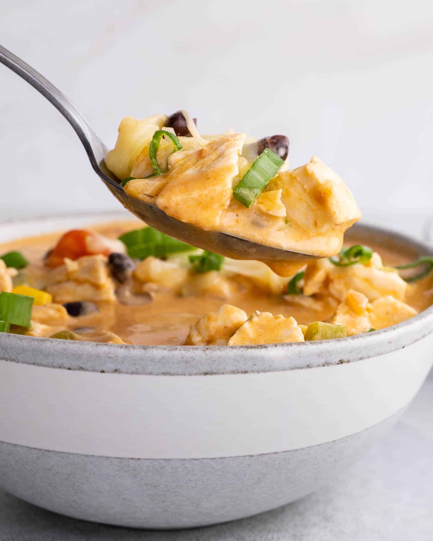a white bowl of cheesy chicken enchilada soup garnished with green onions.