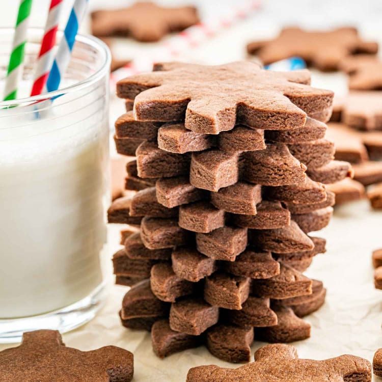a stack of chocolate sugar cookies next to a glass of milk.