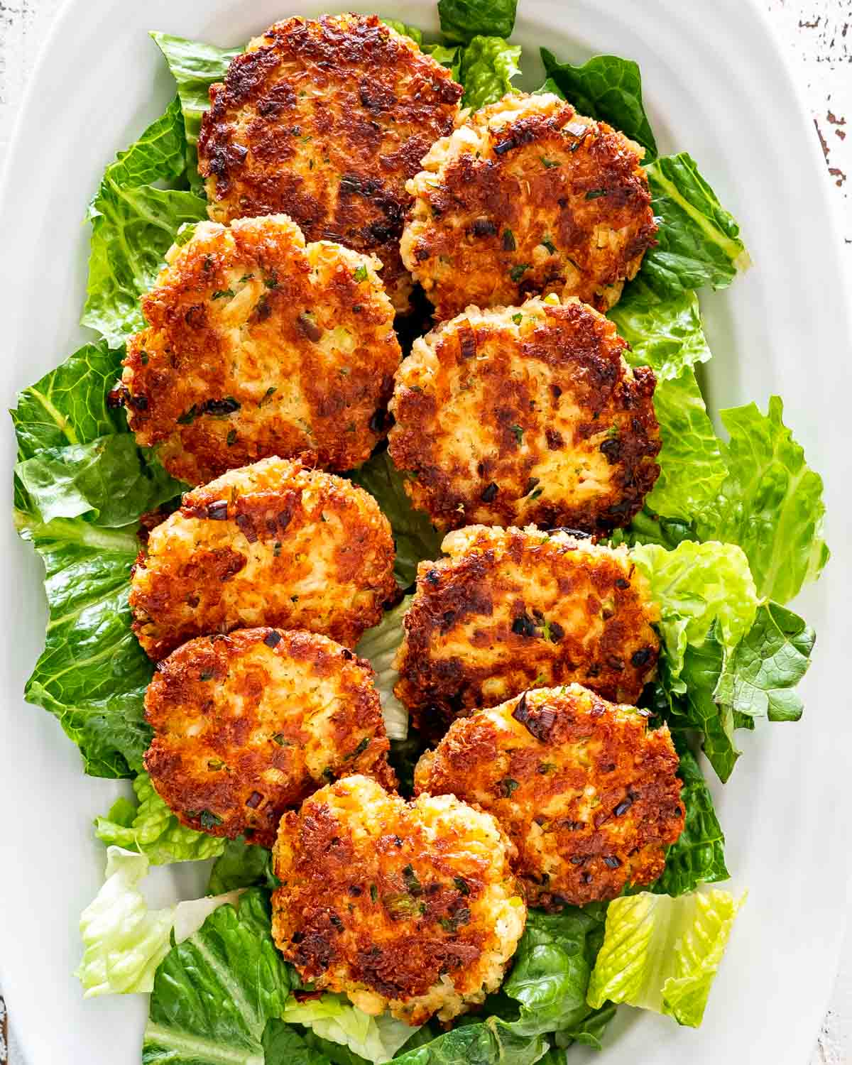 a few crab cakes on a bed of lettuce on a white serving platter.