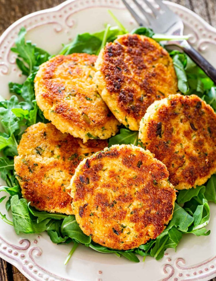 crab cakes on a bed of arugula on a white plate.