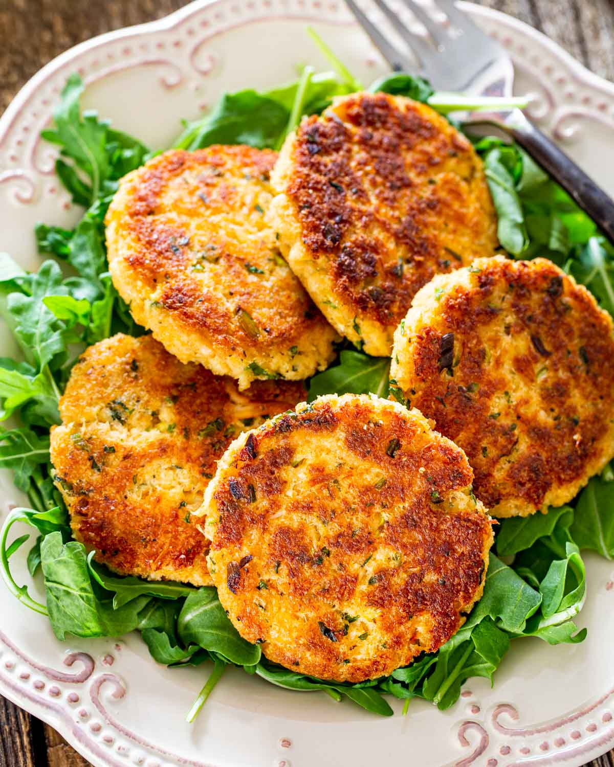 crab cakes on a bed of arugula on a white plate.