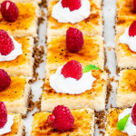 side view shot of creme brulee cheesecake bars topped with whipped cream and raspberries