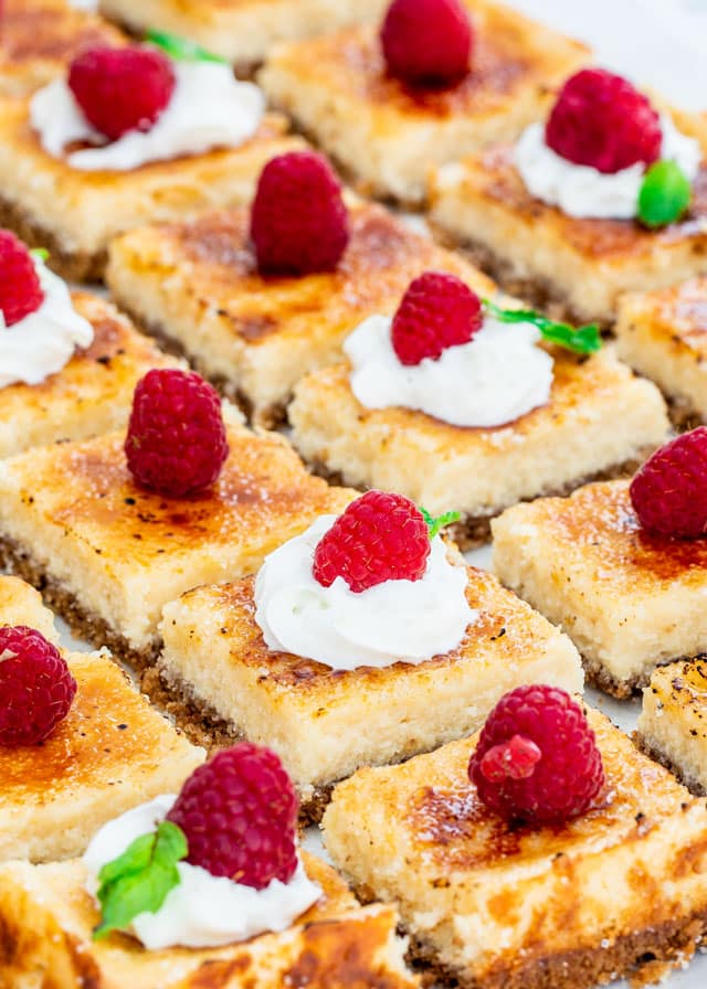 creme brulee cheesecake bars topped with whipped cream and raspberries