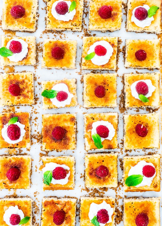 overhead shot of creme brulee cheesecake bars topped with whipped cream and raspberries