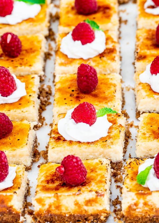 side view shot of creme brulee cheesecake bars topped with whipped cream and raspberries