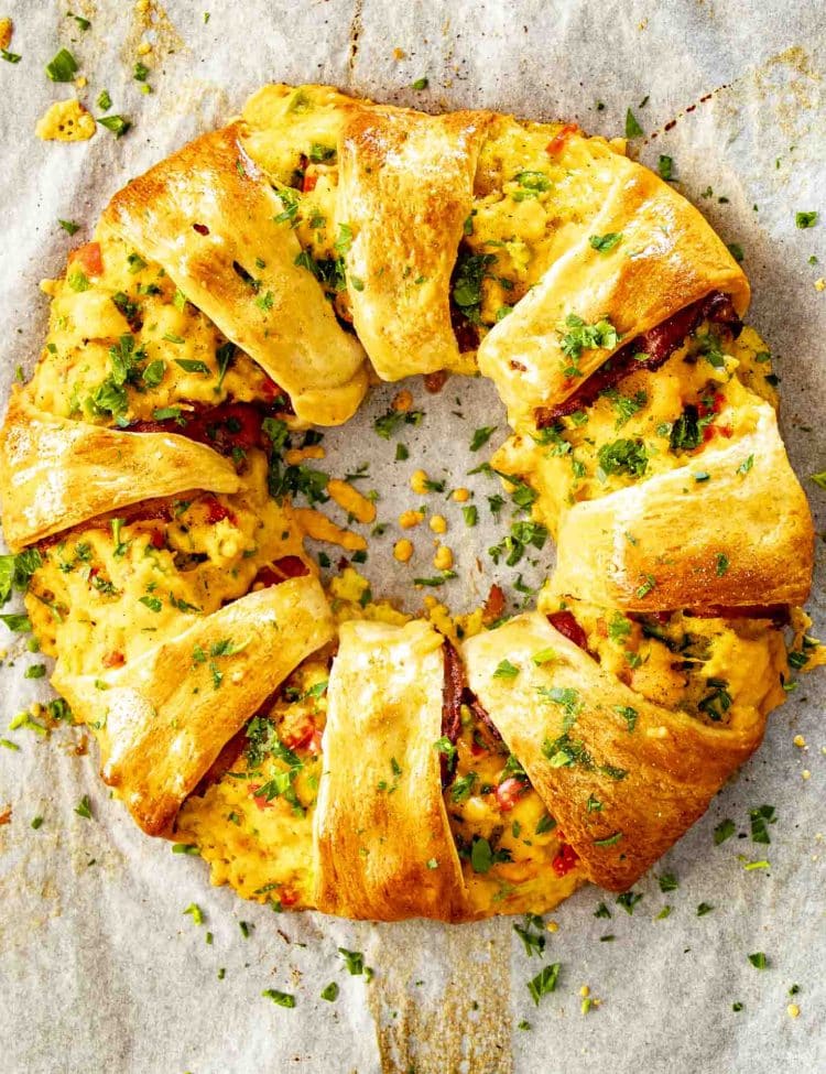 Overhead view of golden crescent breakfast ring filled with scrambled eggs, bacon, cheese, and peppers on parchment paper.