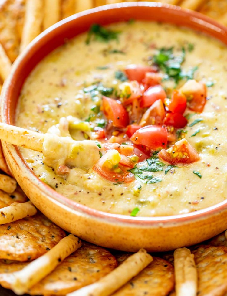 a bowl with queso blanco topped with tomatoes and cilantro surrounded by crackers.