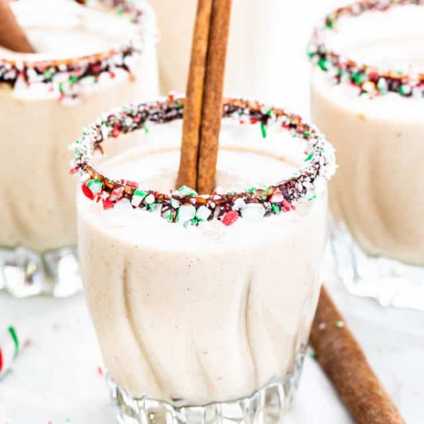 glasses of eggnog in glasses rimmed with chocolate and crushed candy cane pieces, garnished with cinnamon sticks