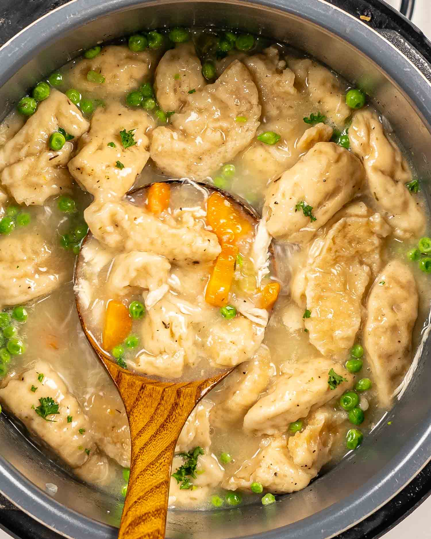 an instant pot with chicken and dumplings and a wooden ladle inside.