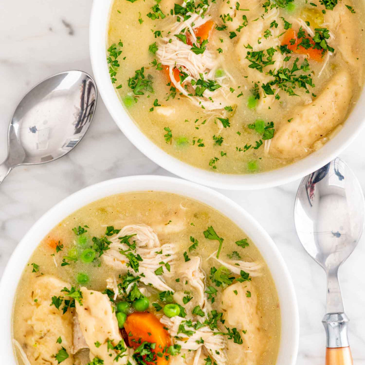 two white bowls with instant pot chicken and dumplings garnished with parsley.