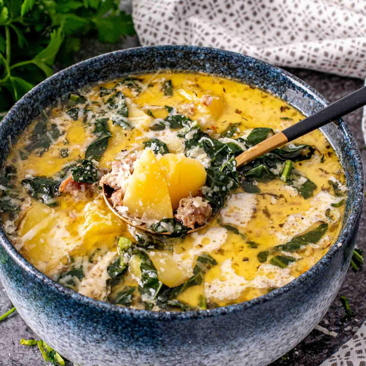 a blue bowl of zuppa toscana that was made in the instant pot.