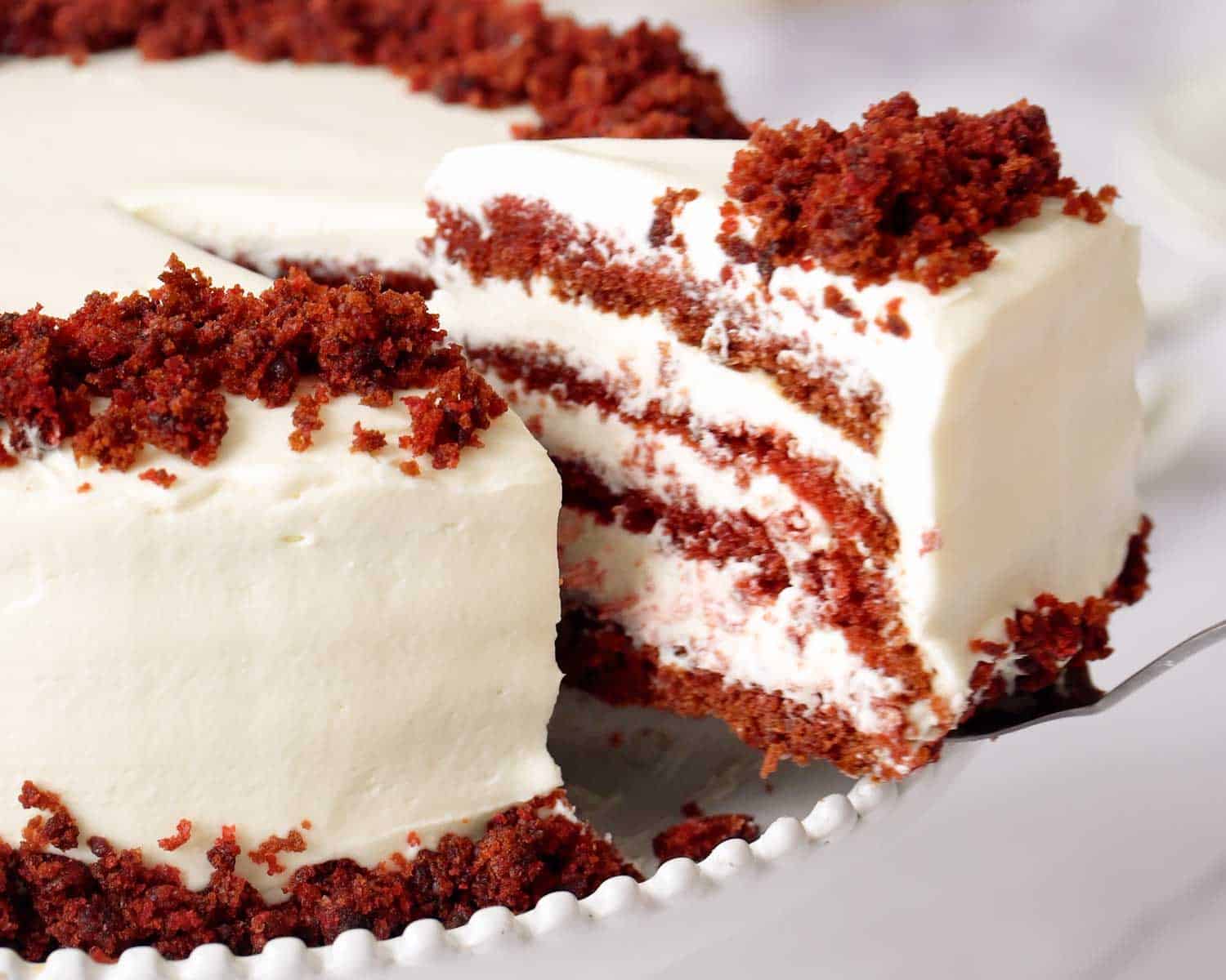 Red velvet cake slice lifted from cake showing multiple layers of cake and cream cheese frosting.