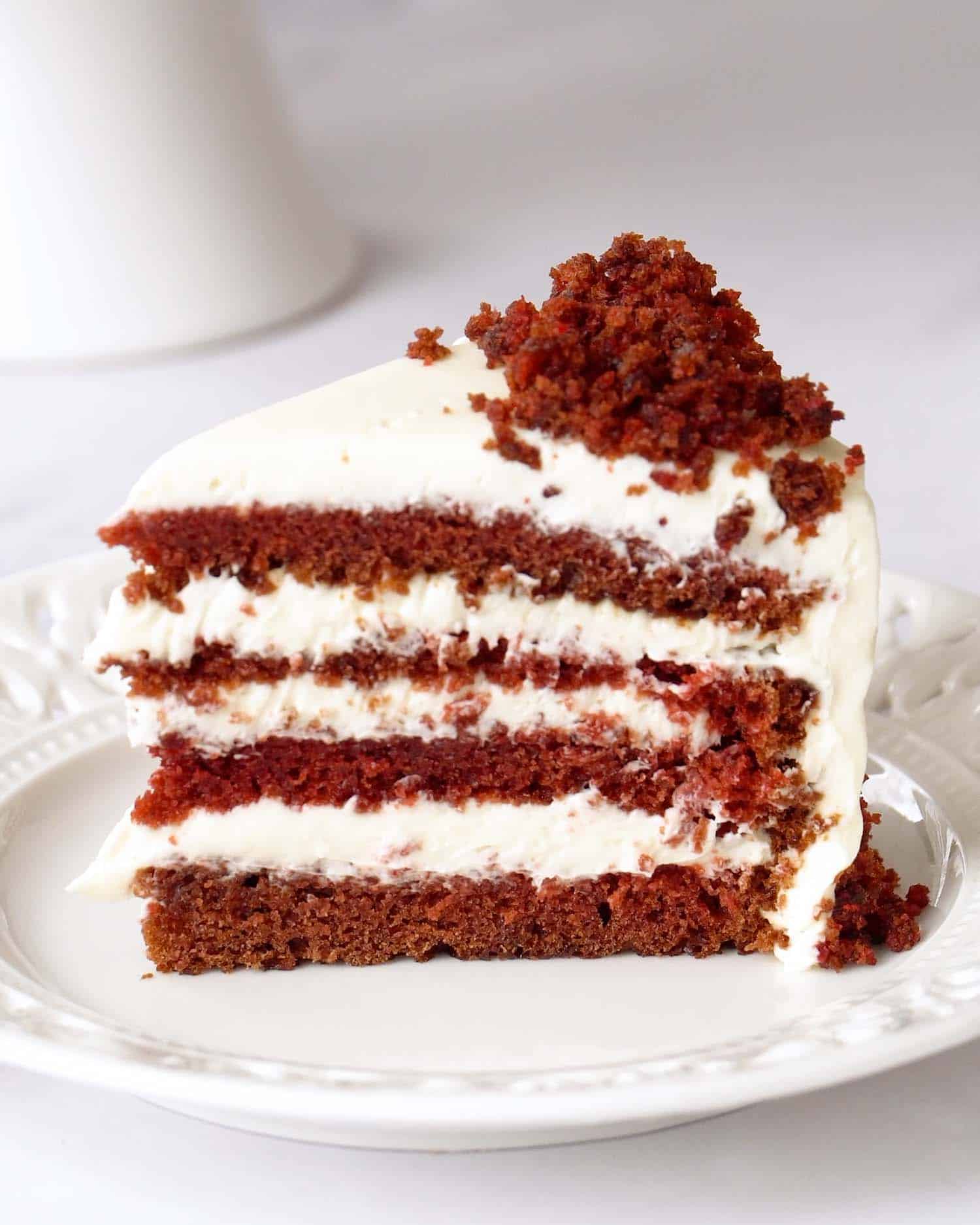 Side view of layered red velvet cake slice with smooth cream cheese frosting and soft tender crumb.