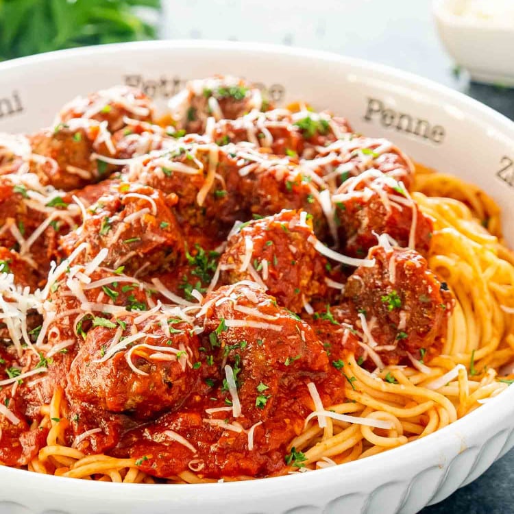 a white bowl full of spaghetti and meatballs garnished with parmesan cheese.