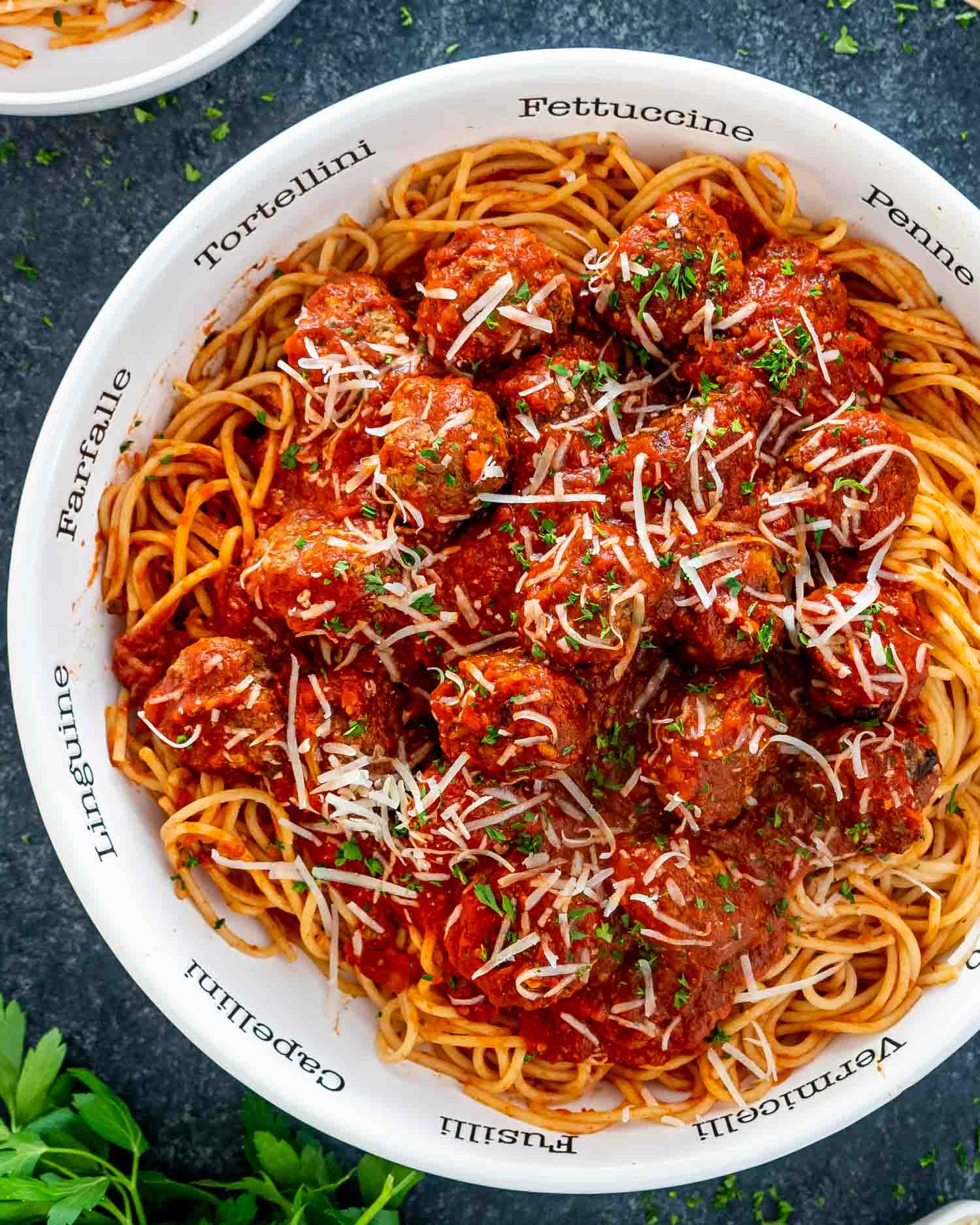 a white bowl full of spaghetti and meatballs garnished with parmesan cheese.