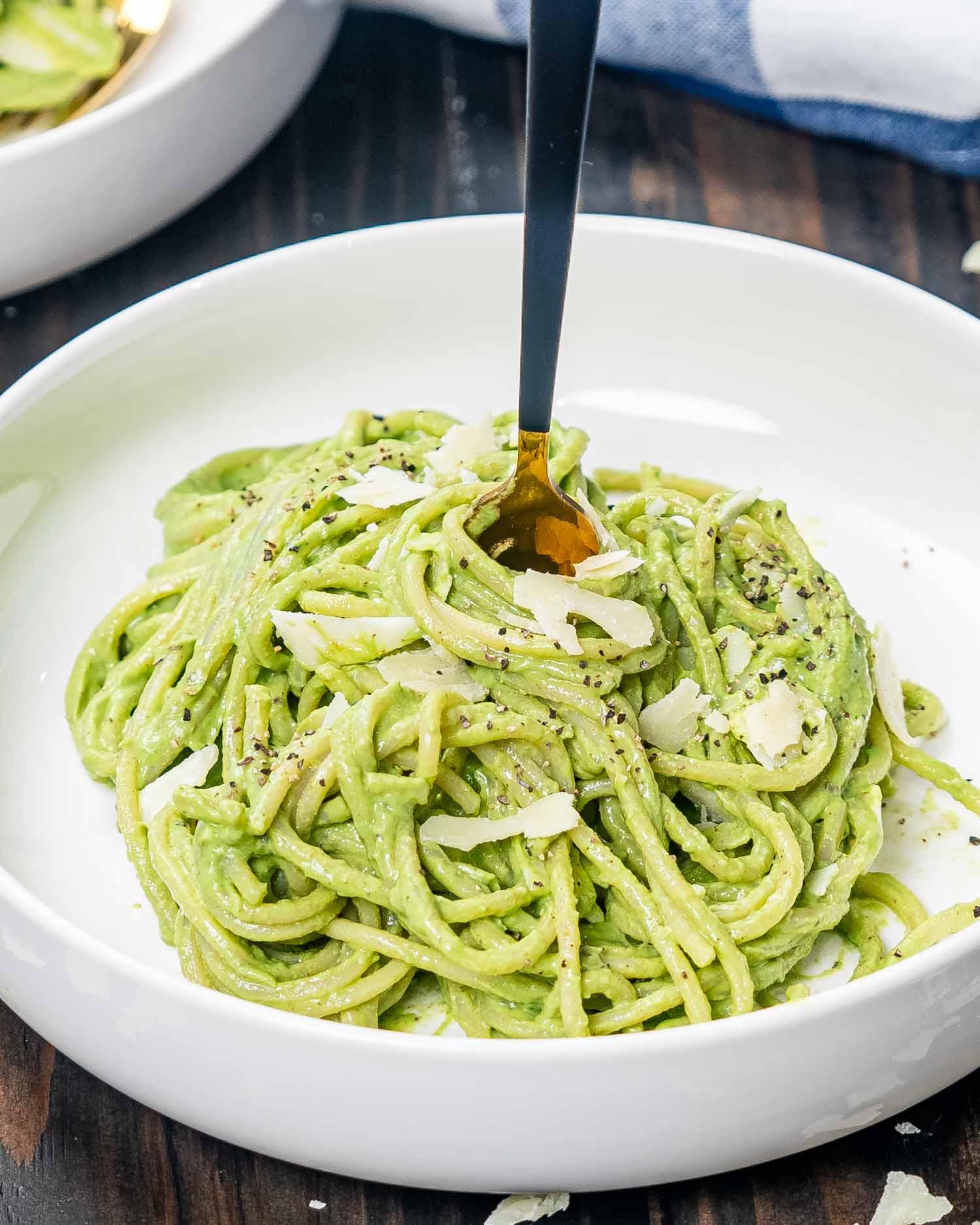 a white bowl with a serving of creamy avocado spinach pasta garnished with parmesan.