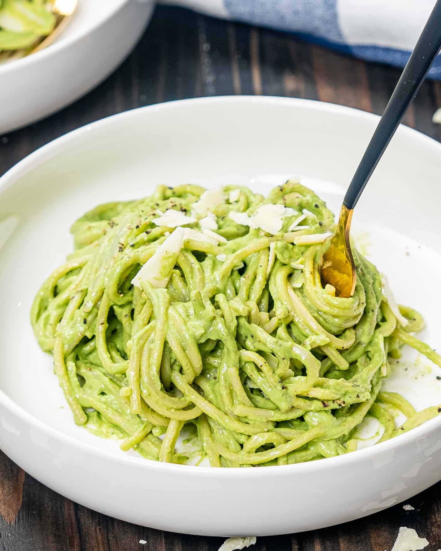 a white bowl with a serving of creamy avocado spinach pasta garnished with parmesan.