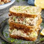 Hearty avocado tuna salad sandwich stacked high with cucumbers and sun-dried tomatoes on multigrain bread.
