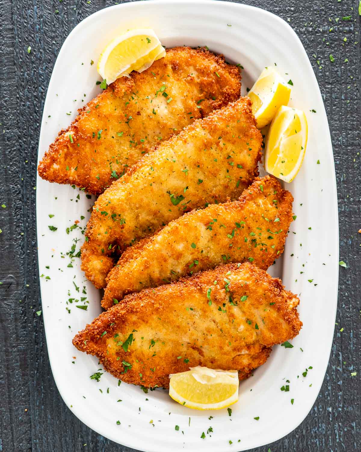 freshly made chicken schnitzel on a platter with lemon wedges.