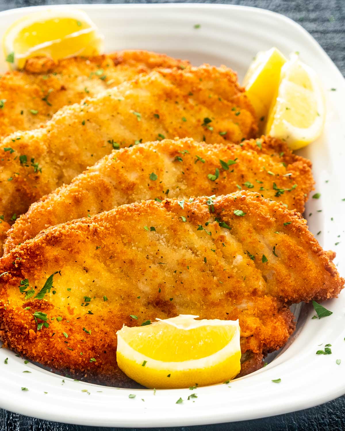 freshly made chicken schnitzel on a platter with lemon wedges.