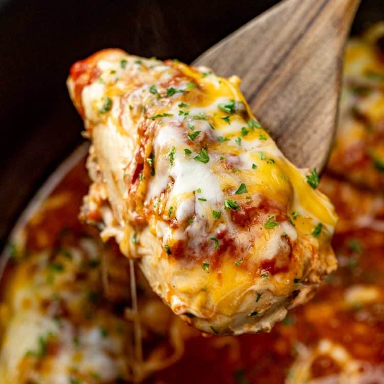 Crockpot salsa chicken breast lifted on a wooden spoon with gooey melted cheese, red salsa, and fresh parsley on top.