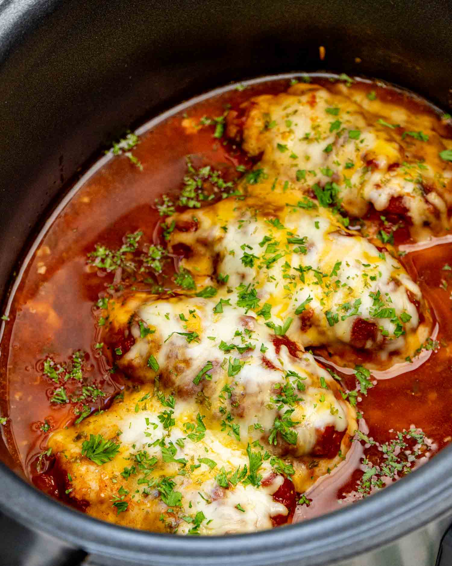 Cheesy crockpot salsa chicken breasts nestled in red salsa sauce and topped generously with melted cheese and chopped fresh parsley.