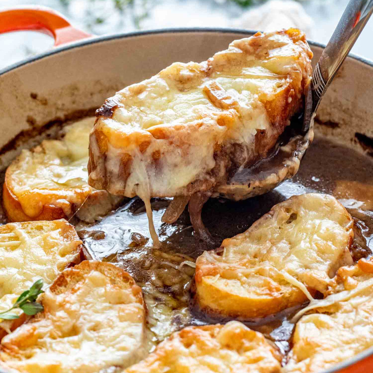 french onion soup in a dutch oven garnished with herbs.