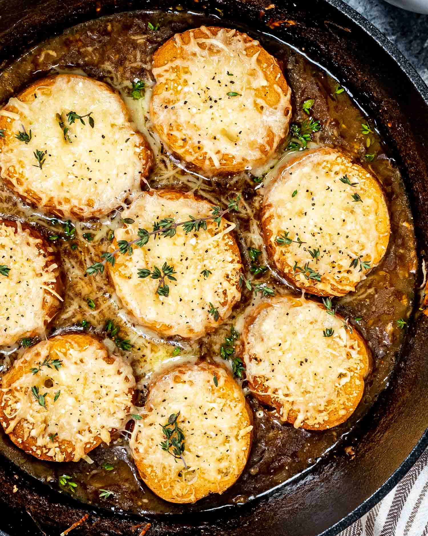 french onion soup in a dutch oven garnished with herbs.