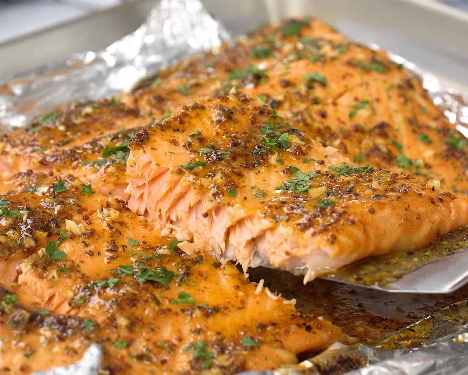 Spatula lifting baked honey mustard salmon from foil showing juicy flaky texture and caramelized honey mustard glaze.