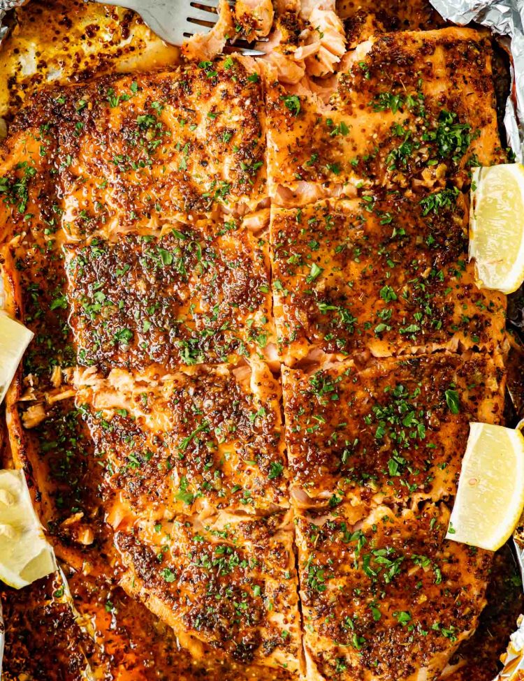 Overhead view of baked honey mustard salmon in foil with caramelized sauce, chopped parsley, and lemon wedges around salmon.