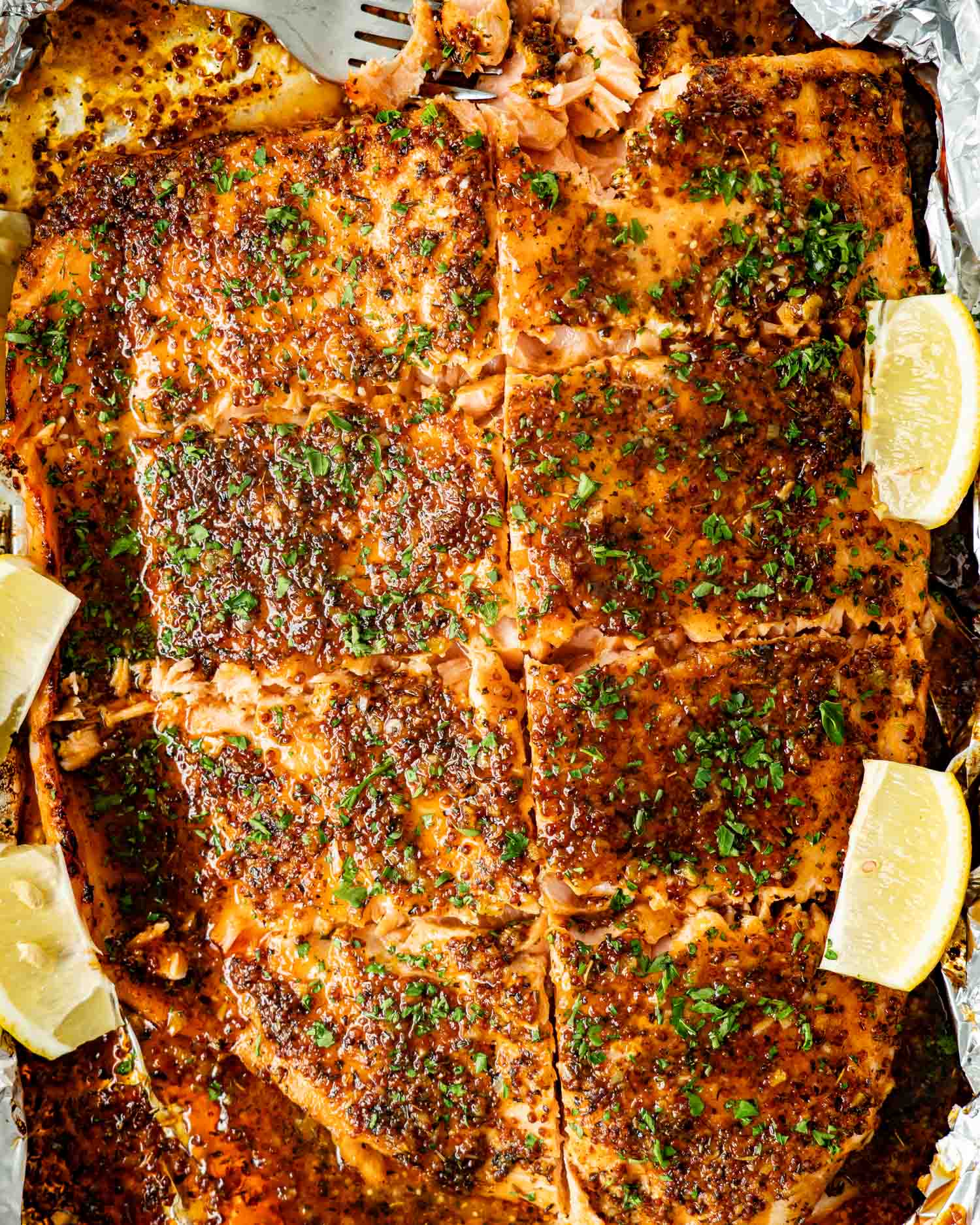 Overhead view of baked honey mustard salmon in foil with caramelized sauce, chopped parsley, and lemon wedges around salmon.
