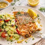Baked honey mustard salmon served with fresh chopped salad, lemon wedge, and sauce drizzled over flaky salmon fillet.