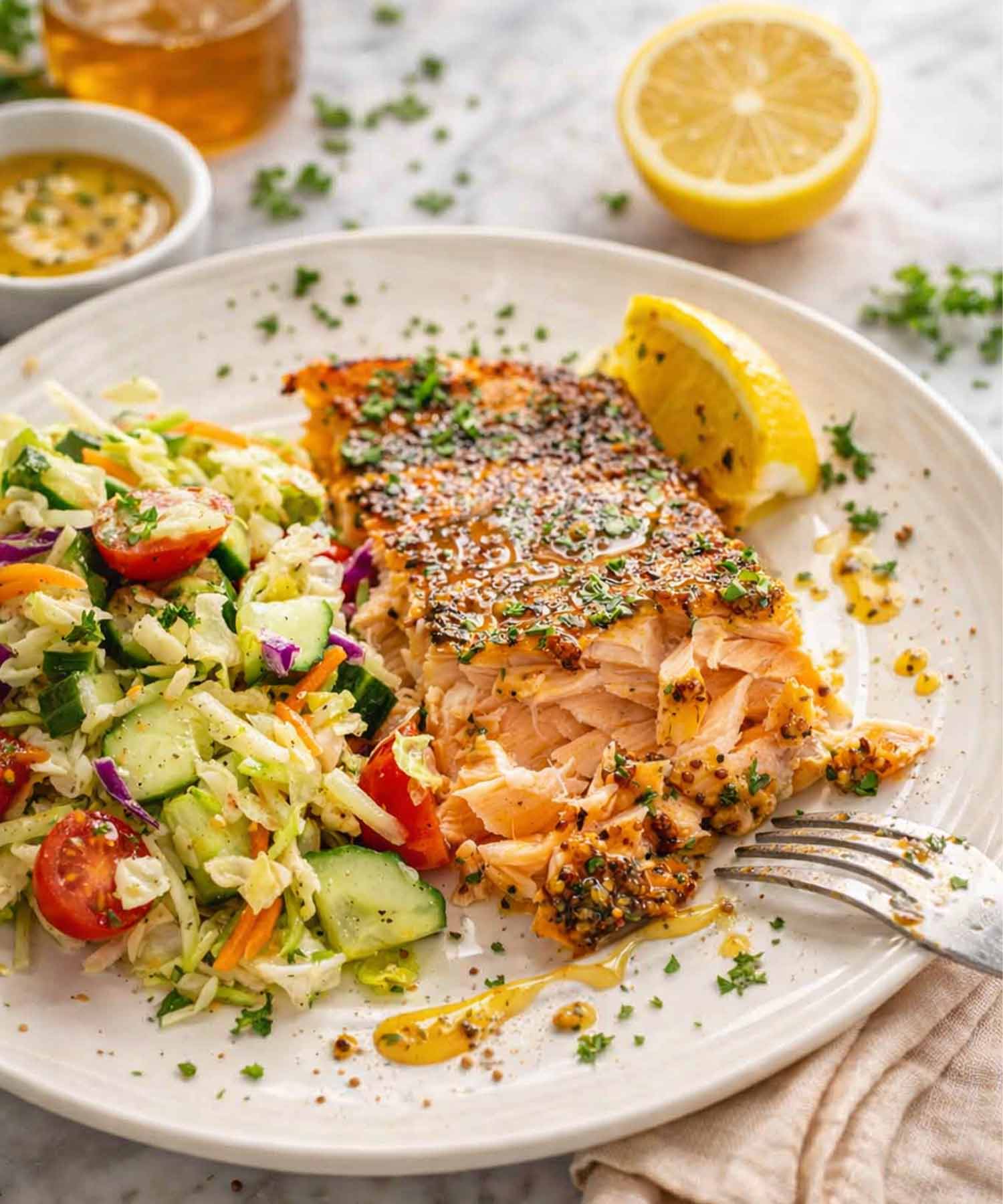 Baked honey mustard salmon served with fresh chopped salad, lemon wedge, and sauce drizzled over flaky salmon fillet.