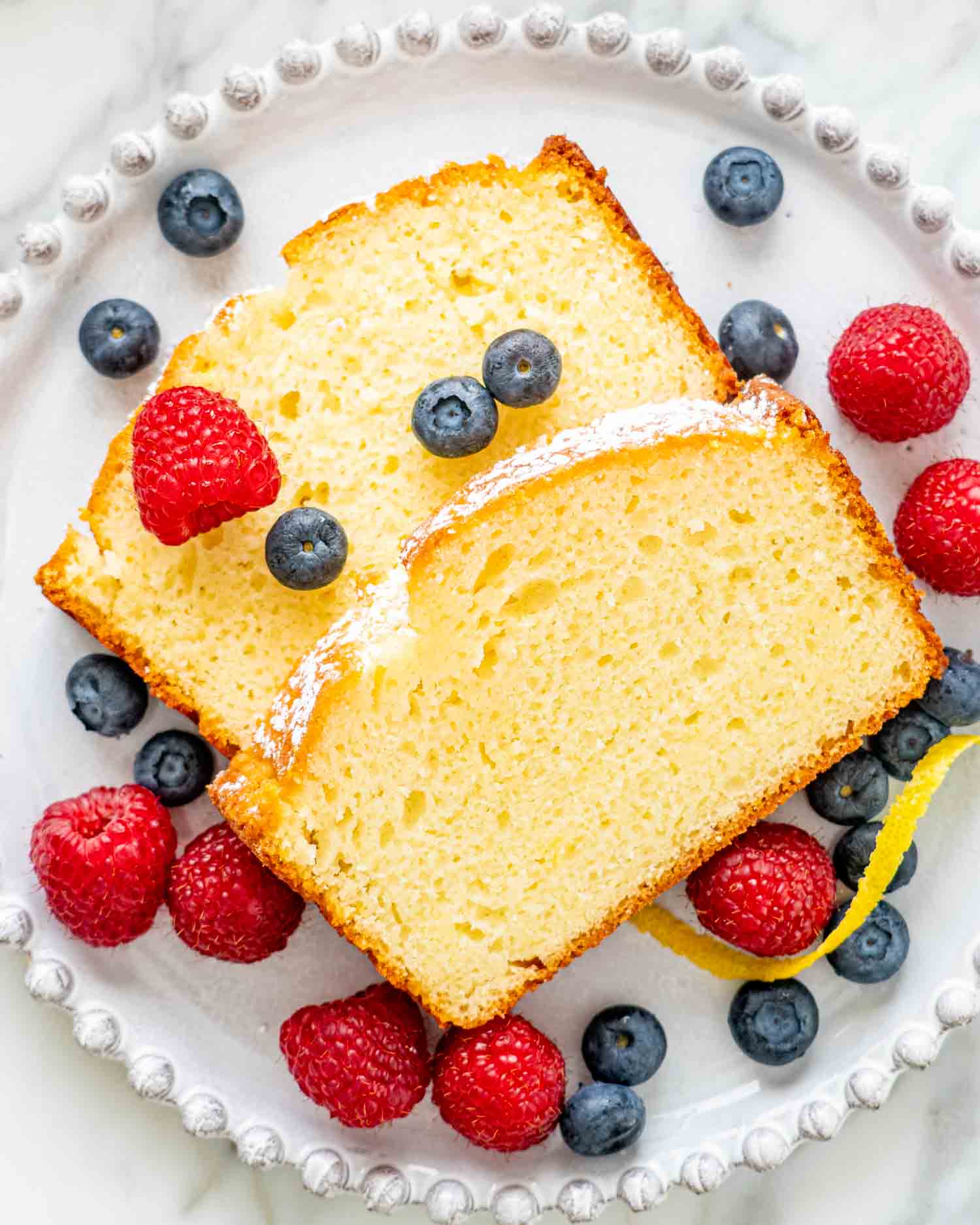 2 slices of lemon yogurt cake on a white plate with berries.