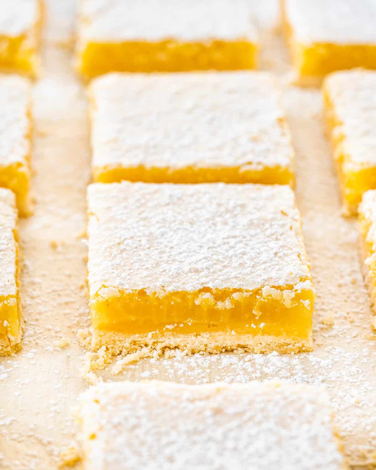 lemon bars cut into squares on parchment paper and dusted with icing sugar.