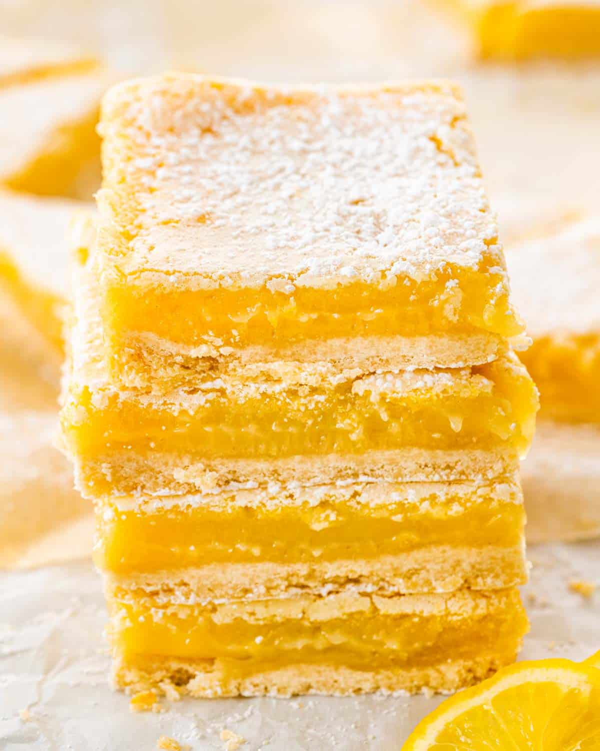 a few lemon bars stacked on top of each other on parchment paper.