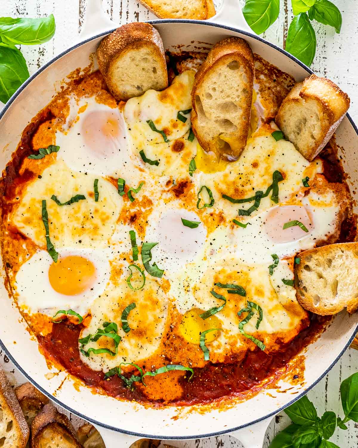 freshly made shakshuka in a beige skillet with some toasted bread.