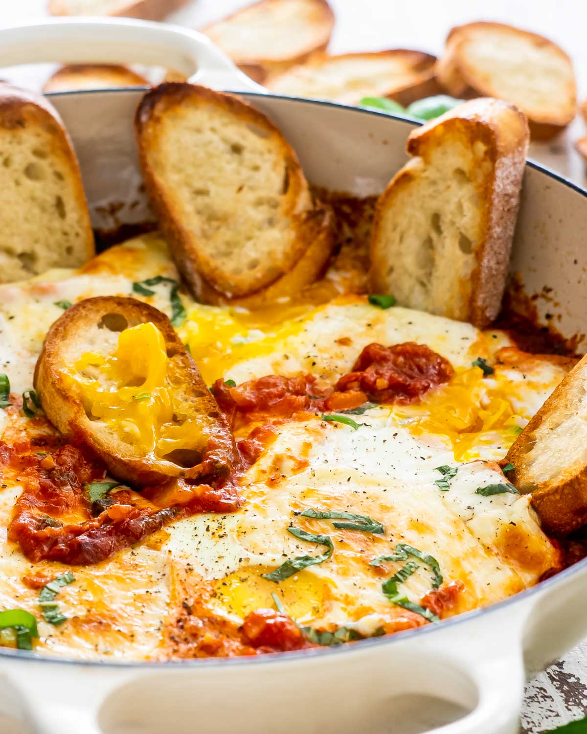 freshly made shakshuka in a beige skillet with some toasted bread.