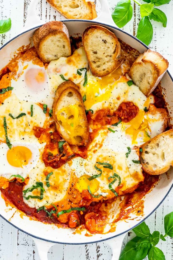 freshly made shakshuka in a beige skillet with some toasted bread.