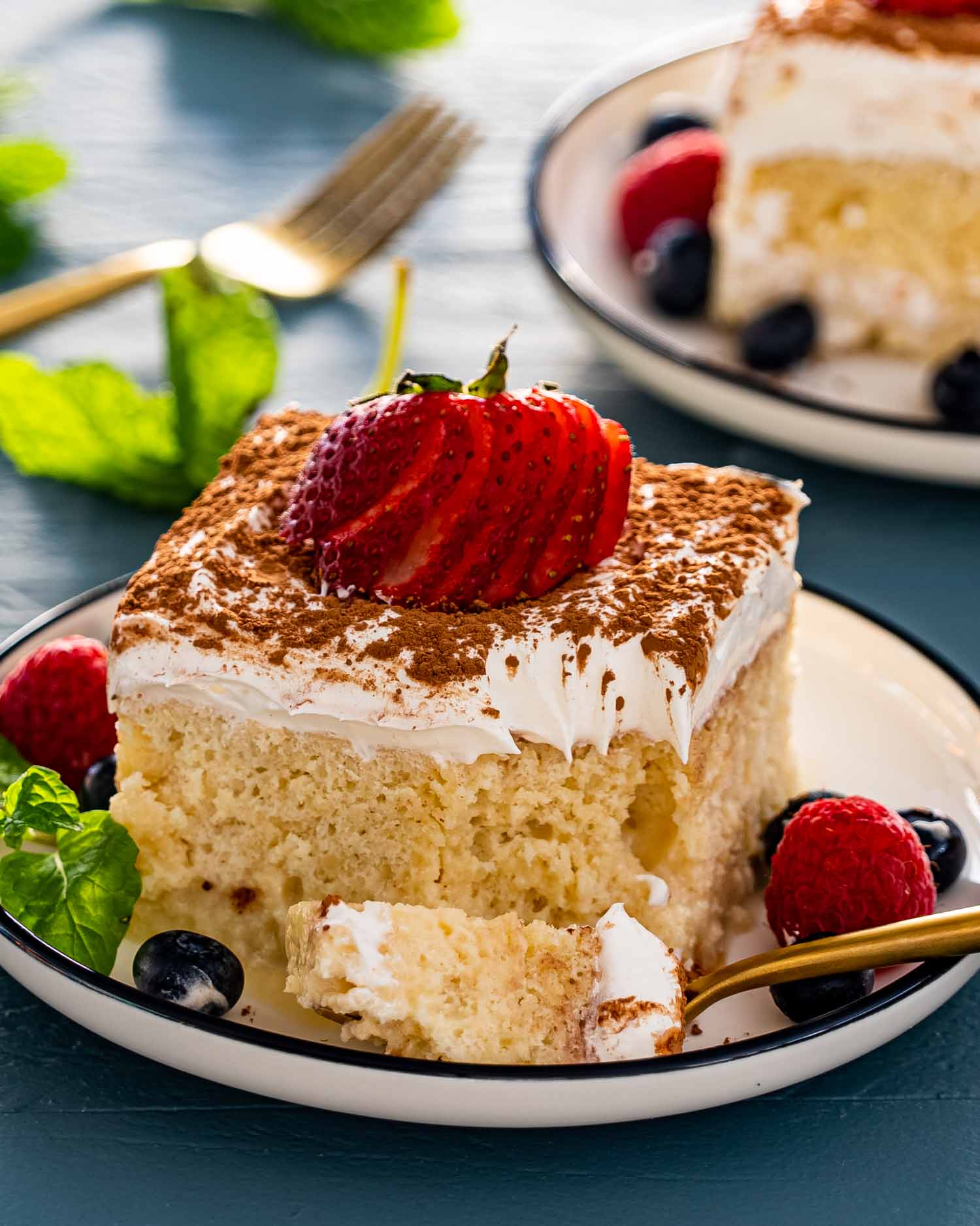 a slice of tres leches cake with a sliced strawberry on top on a white plate.