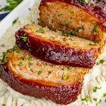 bacon wrapped meatloaf over mashed potatoes on a serving platter.
