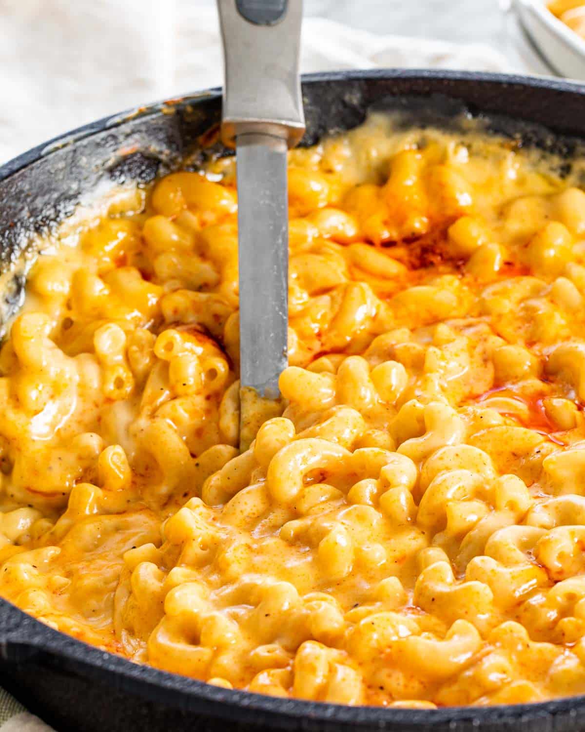 a skillet with mac and cheese and a serving spoon inside.