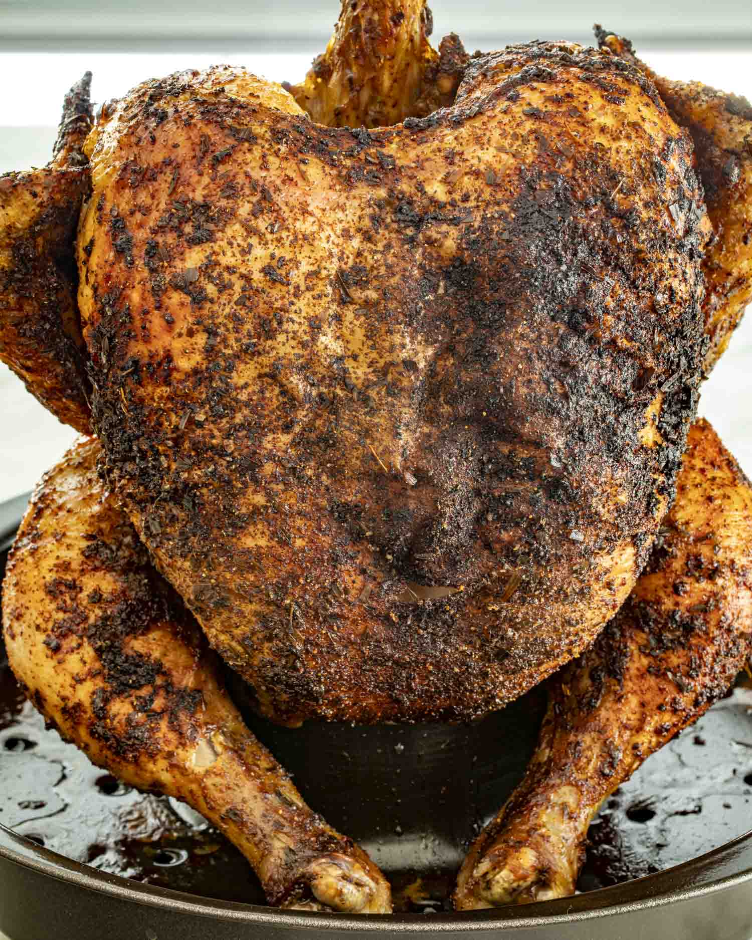 Whole roasted beer can chicken sitting upright in a roasting pan, perfectly golden with herb seasoning.