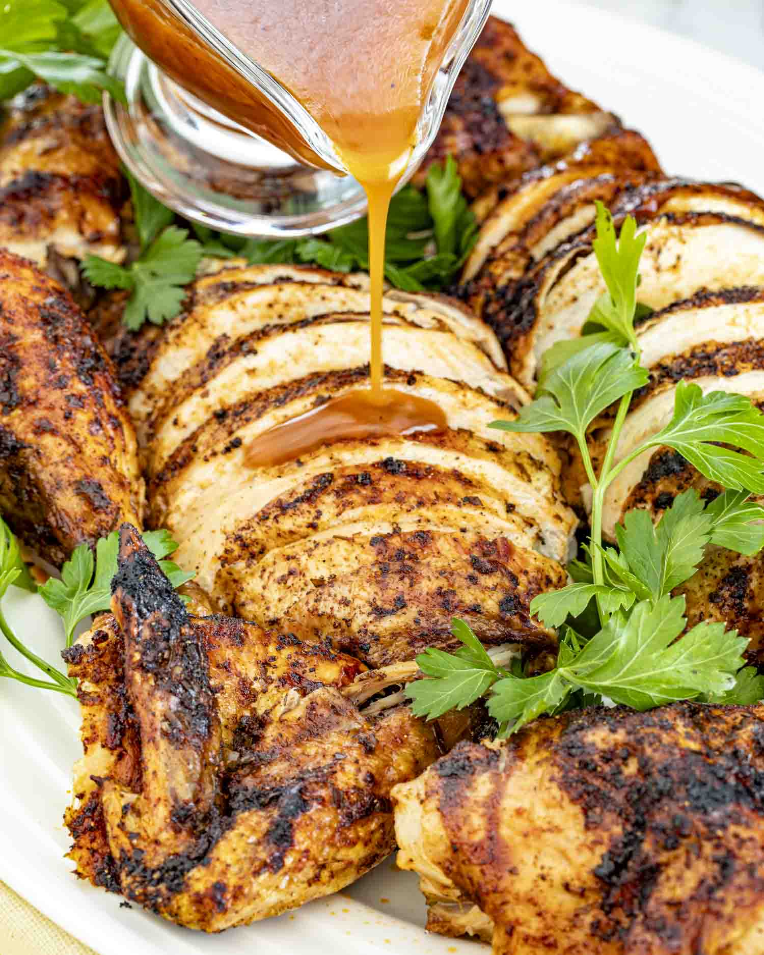 Beer Can Chicken Gravy being poured over sliced beer can chicken on a white platter, surrounded by crispy golden pieces.