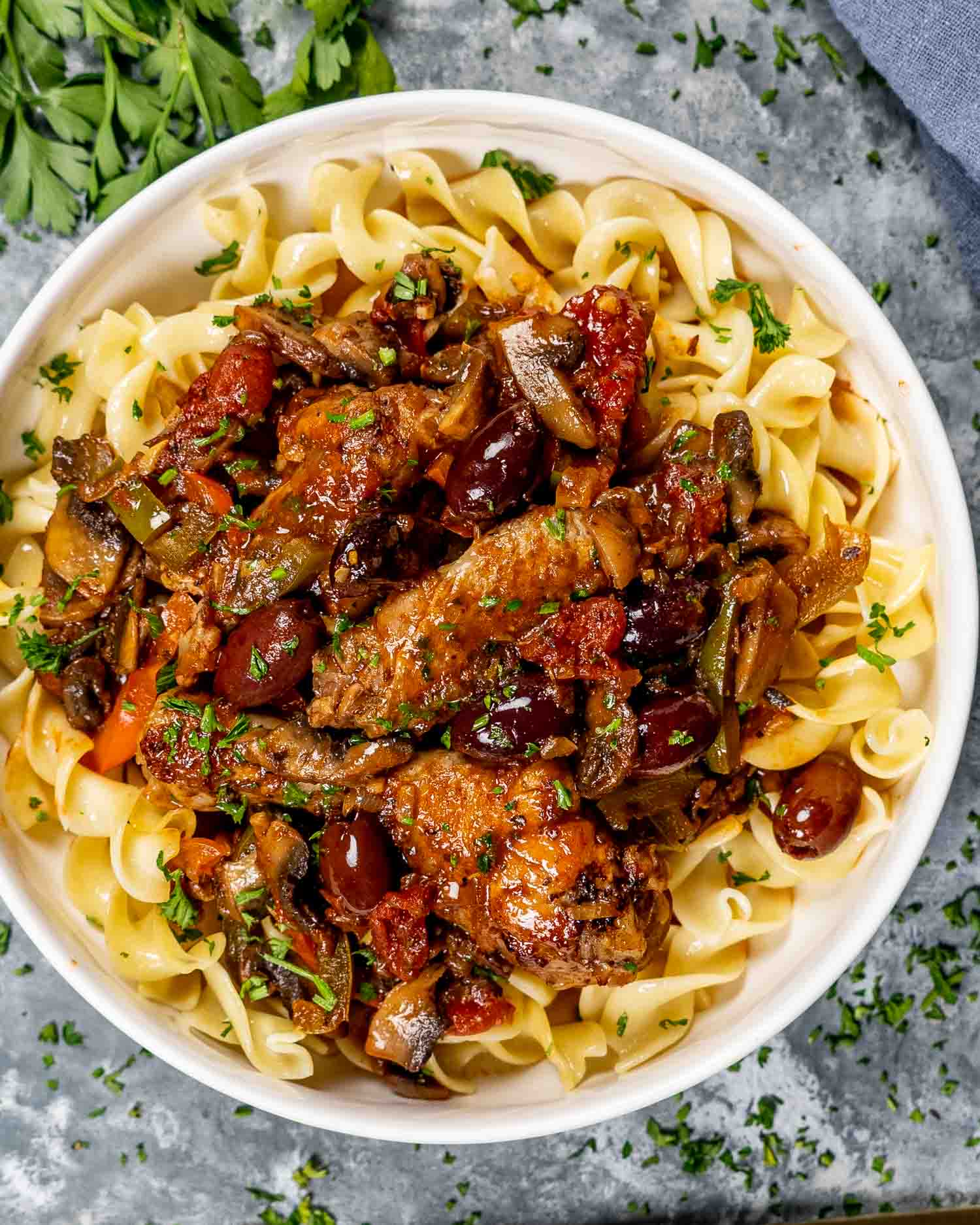 a serving of chicken cacciatore over noodles in a white bowl.